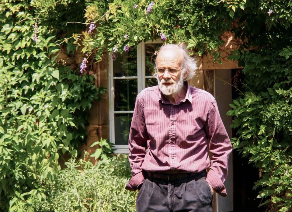Homme âgé barbu devant une maison fleurie
