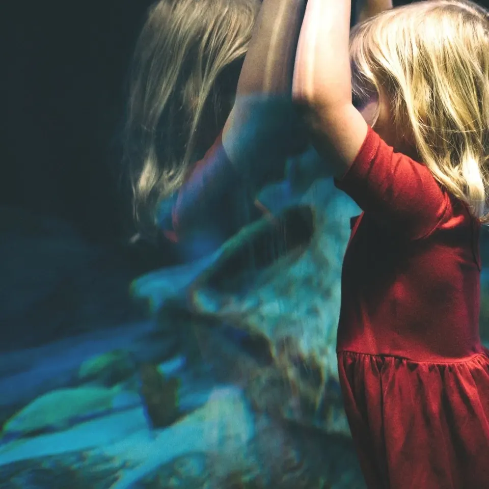 Fillette en robe rouge devant une vitre d'aquarium