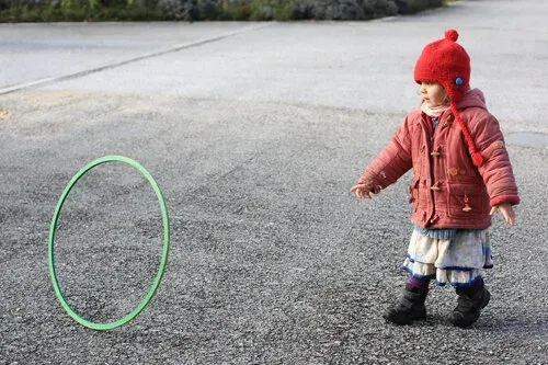 Petit enfant en manteau rouge jouant au cerceau